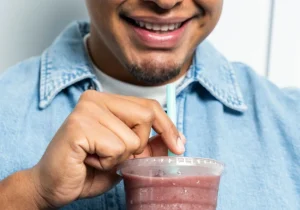 A man smiling while touching the top of his smoothie, representing looking at ingredients